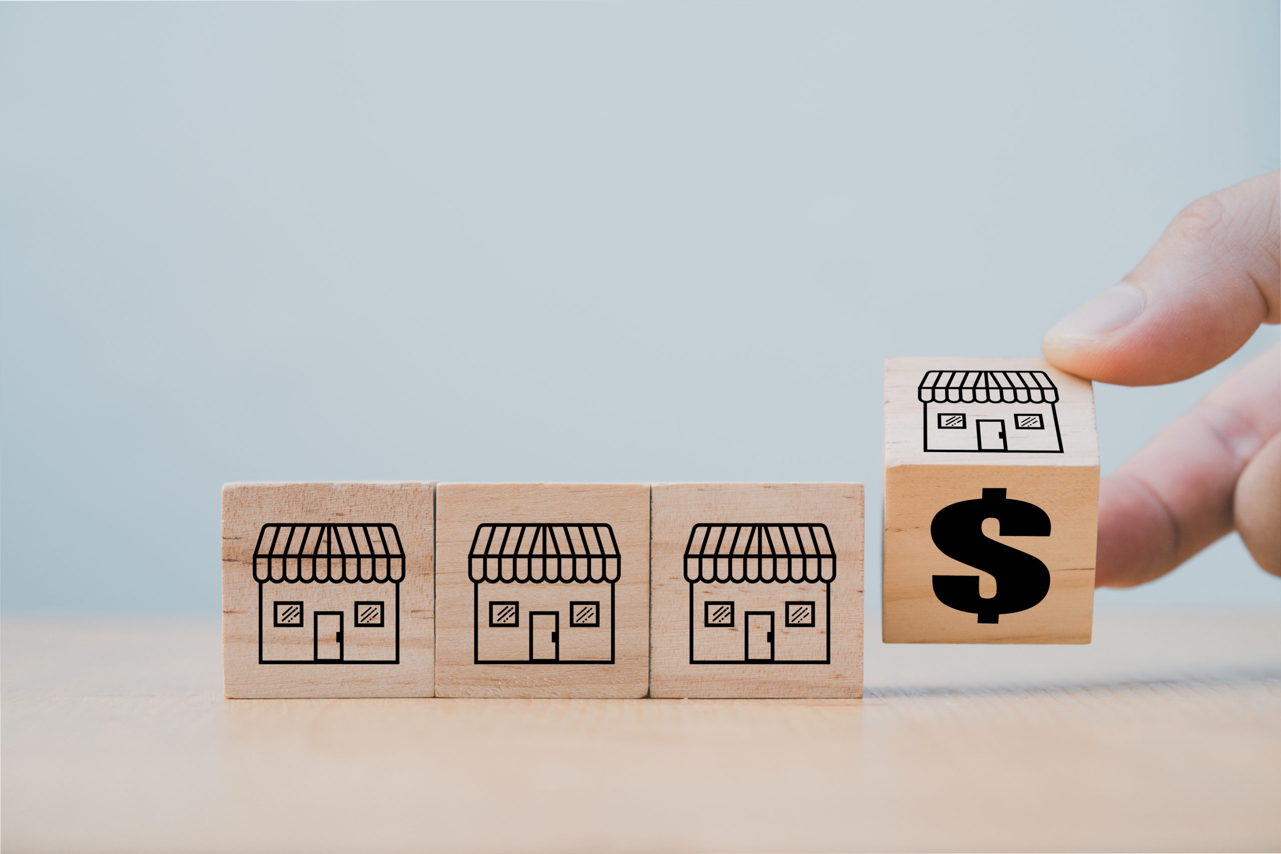 Imagem de quatro cubos de madeira com desenhos de empresas, sendo que o último está sendo "virado" para uma face que representa dinheiro